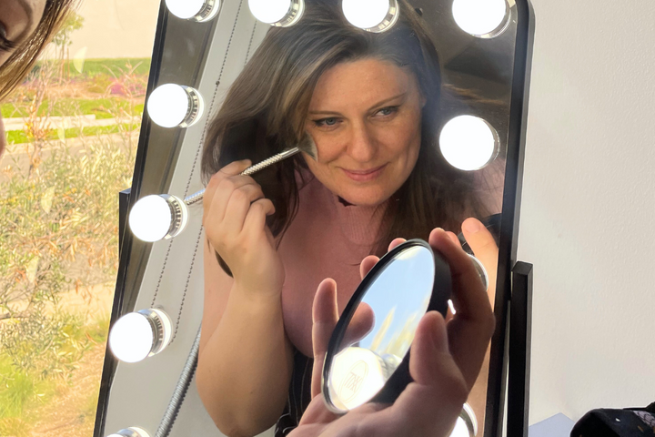 an older woman puts on makeup in front of a mirror – IVC