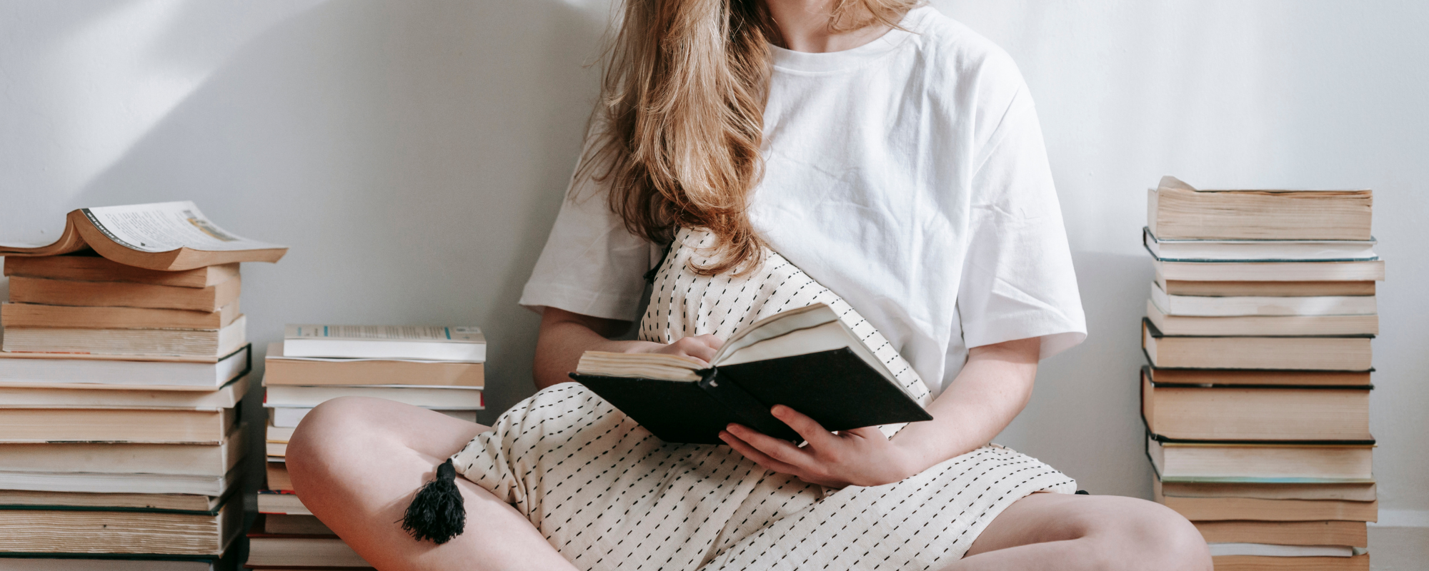 Woman sitting on floor reading next to multiple piles of books — IVC